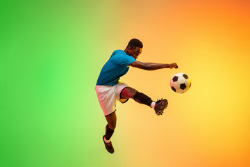 High jumping. Male soccer, football player training in action isolated on gradient studio background in neon light. Concept of motion, action, ahievements, healthy lifestyle. Youth culture.