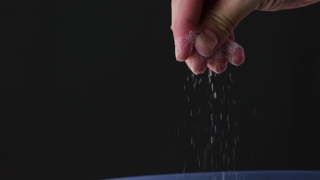 Man's hands are sprinkling salt on food on a black background.