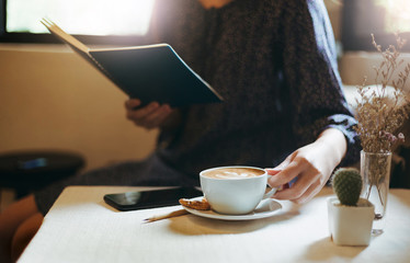 Young asian  woman holding coffee cup to drink while she relaxing and reading book in living room