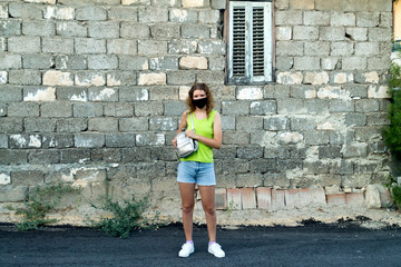 Girl in protective face mask standing in front of old stone house wall