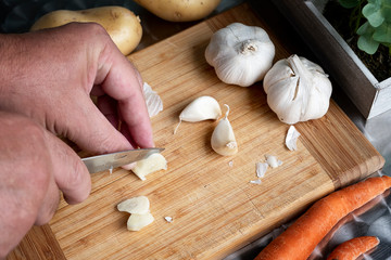 Peeling and cutting garlic on a wooden board. Man's hands.