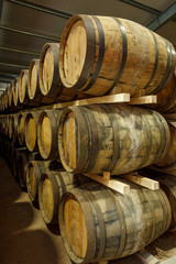 A row of stacks of traditional full whisky barrels, set down to mature, in a large warehouse