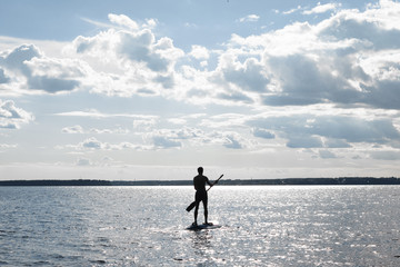 Silhouette of a man Paddling on SUP board in Standing position on a flat warm quiet sea