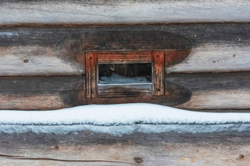 A window in an old wooden building made of boards covered with snow