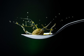 closeup of green olive with splashing oil on a spoon on a dark background - 372275328
