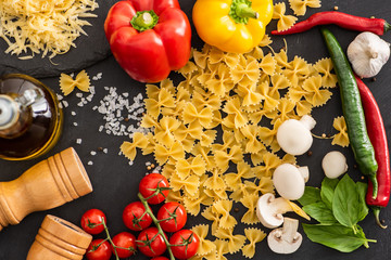 top view of raw Italian farfalle with vegetables and seasoning on black background