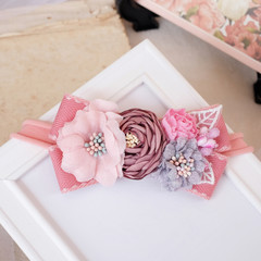 Handmade flower made out of fabric cloth textile in beautiful soft pastel pink theme colors that can be used as hair accessory, decoration, and embellishment placed on white photo frame
