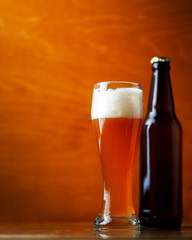 A glass of cold wheat unfiltered beer on a wooden table and a bottle of beer with copy space