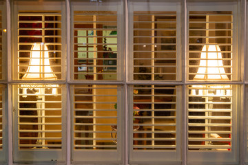 lamps in the windows of a cosy looking home though window shutters
