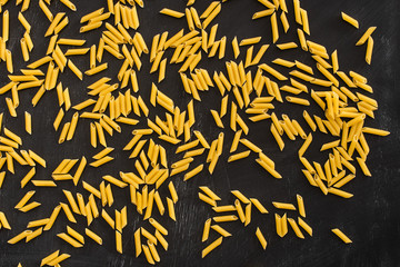 top view of raw penne pasta scattered on black background