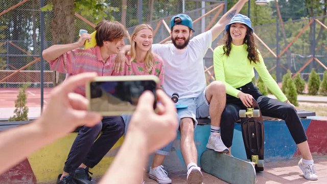 Group of young people multiethnic posing in front of the camera in a modern skate park they holding their skateboard one guy take pictures with the modern smartphone. Shot on ARRI Alexa Mini
