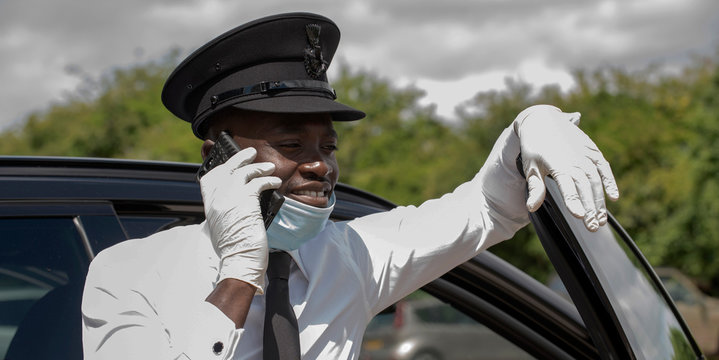 Hampshire, England, UK. 2020. A chauffeur wearing a face mask and protective rubber gloves using a mobile phone during the Covid-19 outbreak,