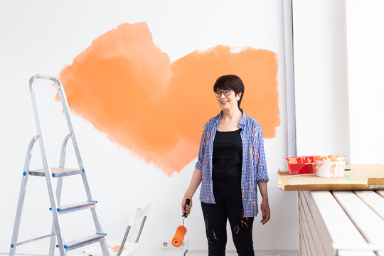 Beautiful middle-aged female painting the wall with paint roller. Portrait of a young beautiful woman painting wall in her new apartment. Redecoration and renovation concept.