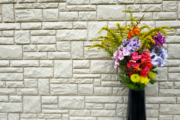 A bouquet of flowers in a vase against a stone wall