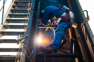 Welder is welding the steel plate by process shielded metal arc welding (SMAW). Welder in blue...