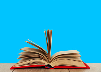 Open book textbook in a red cover on a wooden desk with blue background. Back to school distance home education.Quarantine concept of stay home.