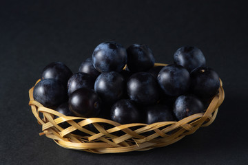 Plum in a wicker basket. Photo on a black background. Summer harvest