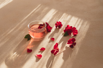 Obraz na płótnie Canvas Glass bowl full of organic rose water and rose petals on the side. Hard sun light on soft peachy colored background