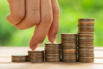 Investor business man finger walking on row of coins stack with blur green nature background. Money saving concept or Business growth concept.