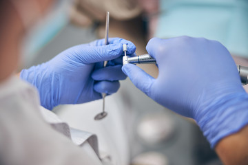 Doctor in blue gloves holding dentist equipment in hands