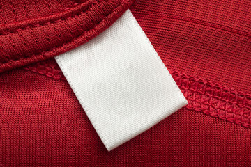 White blank laundry care clothes label on red polyester sport shirt background