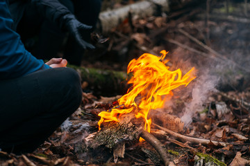 Man warms his hands on fire. Burning wood at evening in the forest. Campfire at touristic camp at nature. Barbeque and cooking outdoor fresh air. Flame and fire sparks on dark abstract background