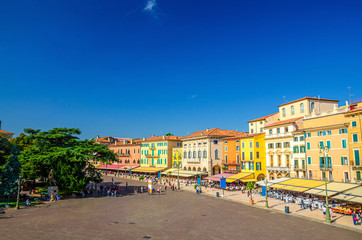 Piazza Bra square aerial view in Verona city historical centre with row of old colorful multicolored buildings cafes and restaurants, green trees and walking tourists, Veneto Region, Northern Italy