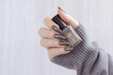Female hand with long nails and gray black manicure with bottles of nail polish