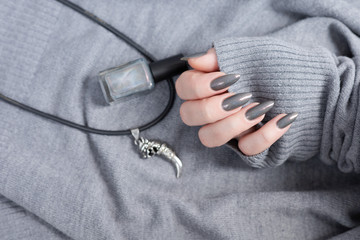 Female hand with long nails and gray black manicure with bottles of nail polish