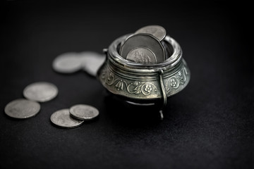 Silver pot full of coins on black background. Leprechaun treasure concept