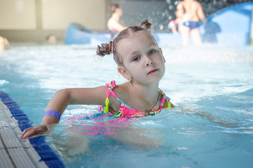 little beautiful girl playing with a foam noodle in a indoor pool. rest in the water park
