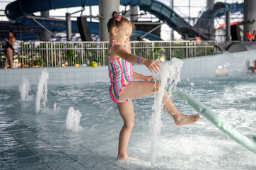little beautiful girl playing with a foam noodle in a indoor pool. rest in the water park