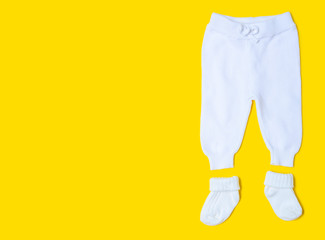 Baby newborn white clothing pants, socks on yellow background, top view