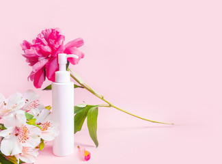 Cosmetic bottle with dispenser with pink peony blossom on pink pastel background. Cosmetics poster or banner design. Fresh modern wallpaper. Advertising banner. Still life advertisement . High quality