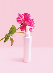 Cosmetic bottle with dispenser with pink peony blossom on pink pastel background. Cosmetics poster or banner design. Fresh modern wallpaper. Advertising banner. Still life advertisement . High quality