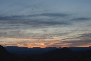 Its right after sunset in southern California desert, with a colorfully illuminated sky, while a mountain range is silhouetted landscape.  The daram created with light and cloud formation . 
