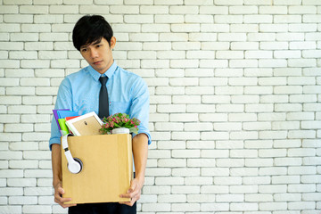 fired dismissled young Asian employee with cardboard brown box filled with his personal belongings in the  business office