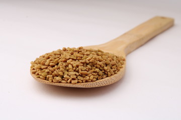 Seeds of fenugreek in wooden spoon on white background closeup