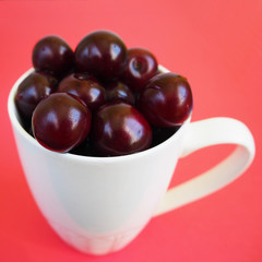 red juicy cherry in a white Cup on a red background side view . ripe summer berries