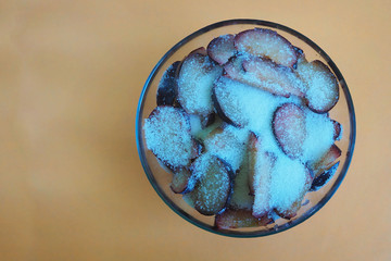 Fototapeta na wymiar cut the plums into slices and sprinkle with white sugar in a clear glass bowl on a beige top view background . seasonal fruits