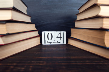 Calendar among books against the background of the chalk board. Concept for Knowledge Day, beginning of the school year. Copy space.