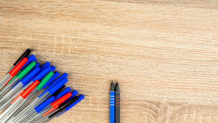 Pile of a lot multi colored plastic ballpoint pens on wooden table. Abstract stationery background. Top view, flat lay. Copy space for text. 16x9 format. Top view. Close-up.