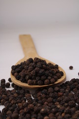 Black pepper in wooden spoon isolated on white background