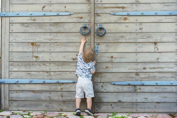Child trying to open huge outside doors. Reach unreachable.