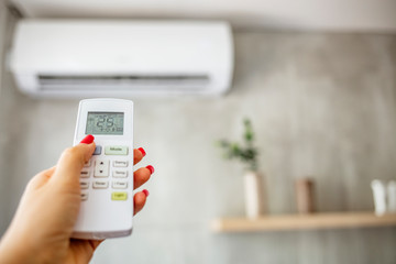 Air conditioner inside the room with woman operating remote controller. / Air conditioner with...