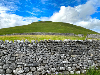 Fototapeta na wymiar The high hill, above Gordale Scar, with a dry stone wall, and field in the foreground in, Malham, Skipton, UK