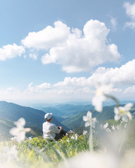 Fototapeta premium A tourist in white clothes sits in a mountain meadow covered with white narcissus flowers. Carpathian mountains, Europe. Landscape photography