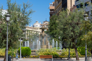 Fototapeta na wymiar View of a central square in Granada with a fountain, lampposts and wooden benches