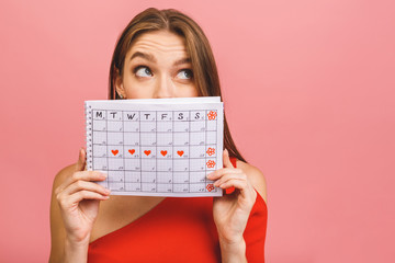 Portrait of a funny young girl hiding behind a periods calendar isolated over pink background.