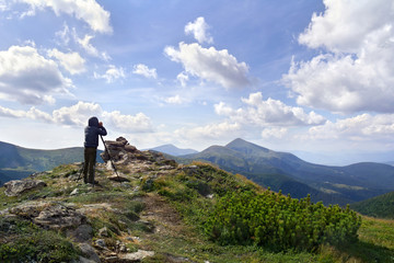 Young photographer man standing on top of cliff taking pictures of the ridge mountain range of Chernogor in Ukraine. Carpathian summer mountains